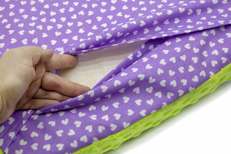 May include: A purple cushion with a white heart pattern on the fabric. The cushion is filled with a white, fluffy material. The cushion has a green, textured backing.