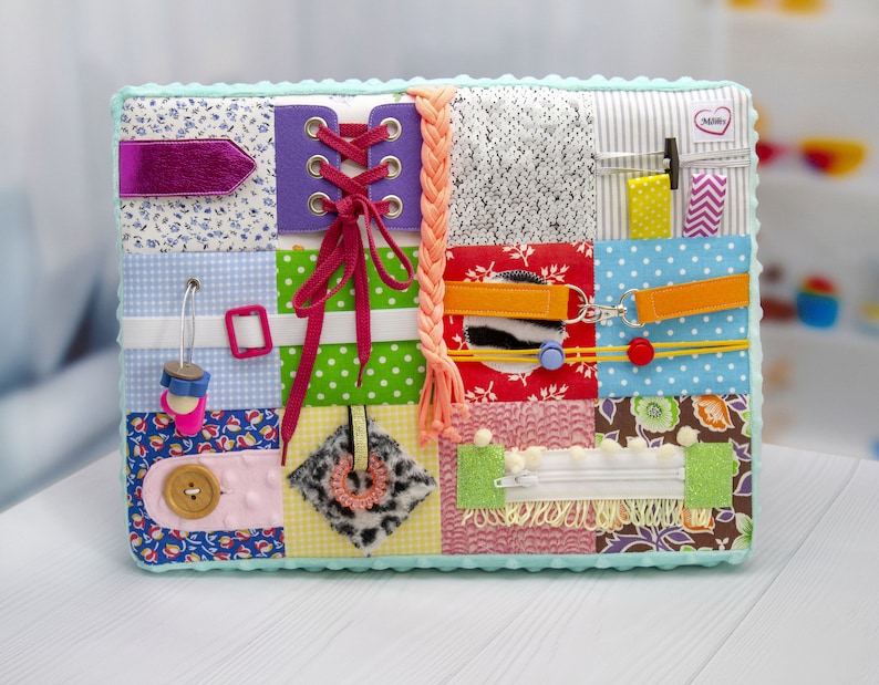 May include: A multi-colored fabric activity book with various textures and features for babies and toddlers. It includes a zipper, buttons, laces, and a variety of fabrics.