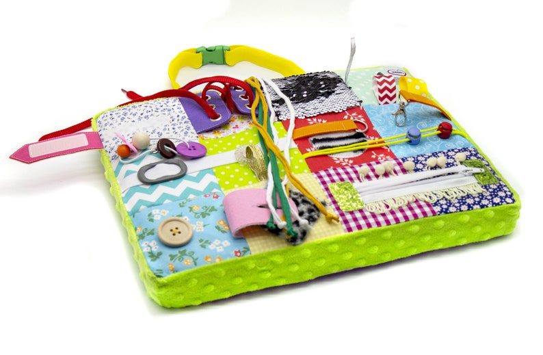 May include: A multi-colored fabric activity mat with various textures and features for babies and toddlers. It includes a zipper, buttons, laces, ribbons, and a tag. The mat is green with white polka dots.
