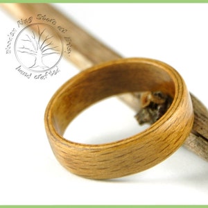 May include: A close-up of a wooden ring, made from natural wood, with a light brown color. The ring is resting on a branch.