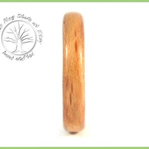May include: A close-up of a wooden ring with a natural wood grain pattern. The ring is a light brown color and has a smooth, polished finish.