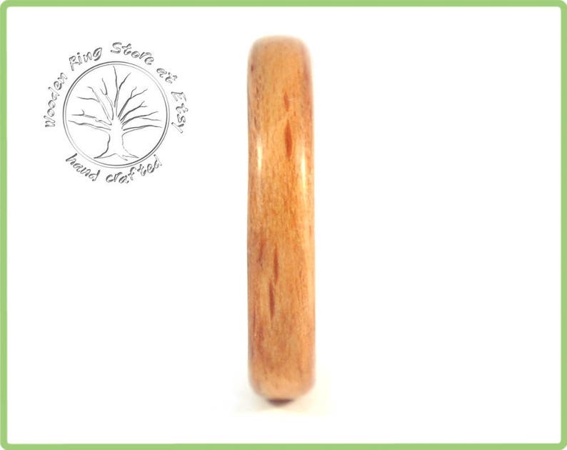 May include: A close-up of a wooden ring with a natural wood grain pattern. The ring is a light brown color and has a smooth, polished finish.