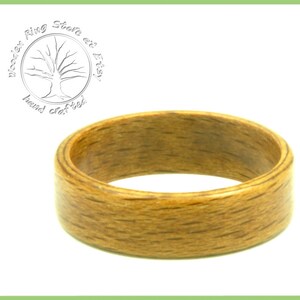 May include: A close-up of a wooden ring with a natural wood grain finish. The ring is a light brown color and has a smooth, polished surface.