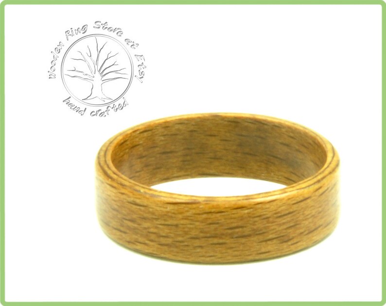 May include: A close-up of a wooden ring with a natural wood grain finish. The ring is a light brown color and has a smooth, polished surface.