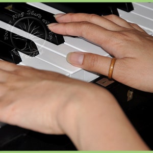 May include: A person's hands playing a piano keyboard. The person is wearing a brown wooden ring on their right thumb.