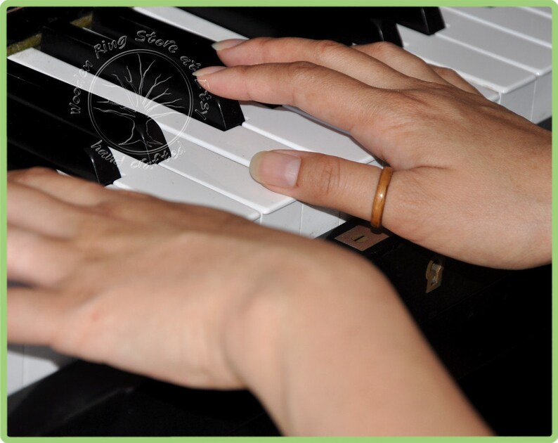 May include: A person's hands playing a piano keyboard. The person is wearing a brown wooden ring on their right thumb.