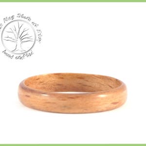 May include: A close-up of a wooden ring with a natural wood grain finish. The ring is smooth and polished, and it has a warm, natural color.