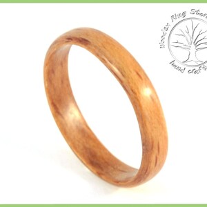 May include: A close-up of a wooden ring with a natural wood grain pattern. The ring is a light brown color and has a smooth, polished finish.