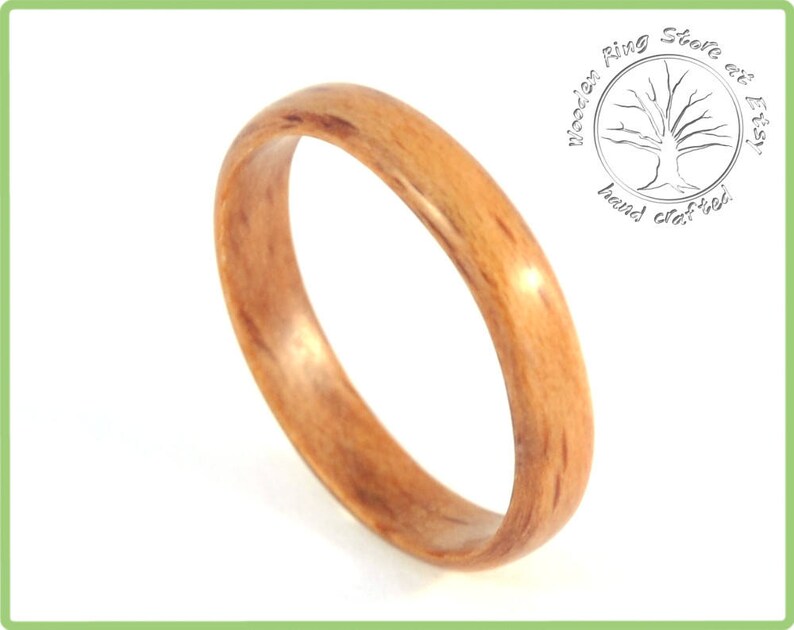 May include: A close-up of a wooden ring with a natural wood grain pattern. The ring is a light brown color and has a smooth, polished finish.