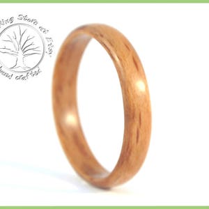 May include: A close-up of a wooden ring with a natural wood grain pattern. The ring is a light brown color and has a smooth, polished finish.
