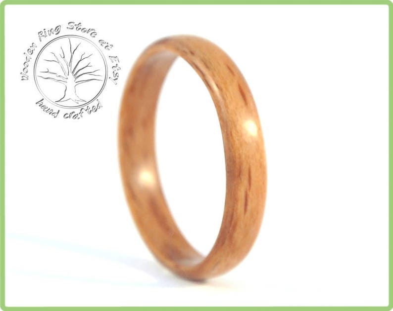 May include: A close-up of a wooden ring with a natural wood grain pattern. The ring is a light brown color and has a smooth, polished finish.