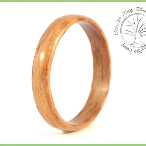May include: A close-up of a wooden ring with a natural wood grain pattern. The ring is smooth and polished, with a warm brown color.