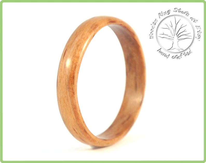 May include: A close-up of a wooden ring with a natural wood grain pattern. The ring is smooth and polished, with a warm brown color.