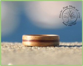 May include: A wooden ring with a natural wood grain pattern and a reddish-brown stripe. The ring is handcrafted and made from wood.