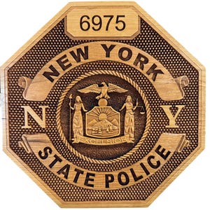 May include: A wooden octagonal sign with the text "NEW YORK STATE POLICE" and the number "6975" in the top center. The sign features the New York State seal with the words "EXCELSIOR" in the center.