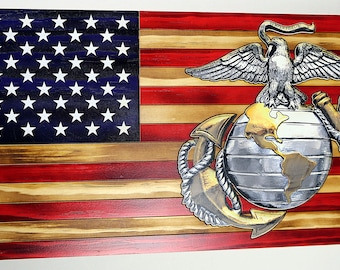 May include: A wooden American flag with a distressed finish, featuring the Marine Corps emblem in the bottom right corner. The emblem is a silver globe with a gold anchor and eagle.