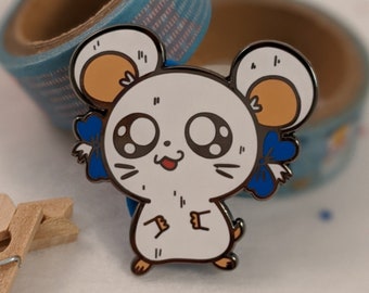 Puede incluir: Pin de esmalte blanco de un ratón de dibujos animados con ojos grandes, una pequeña lengua rosa que sobresale y lazos azules en las orejas. El ratón está de pie sobre sus patas traseras con las patas delanteras en el aire.