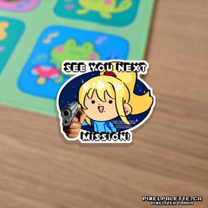 May include: A sticker featuring a cartoon character with blonde hair holding a gun, with the text "SEE YOU NEXT MISSION!". The character is set against a starry background. The sticker has a white border and is on a wooden surface.