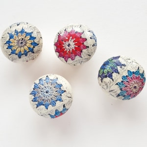 May include: Four spherical decorative knobs with floral patterns. Each knob has a different colour scheme: blue and yellow, red, blue and green, and blue and pink. The knobs have a textured, off-white background.