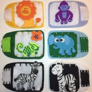 Pode incluir: Seis patches de feltro com diferentes desenhos de animais. Os patches são amarelos, azuis, verdes, brancos, pretos e roxos. Os animais são um leão, um macaco, um camaleão, um elefante, uma zebra e uma zebra.