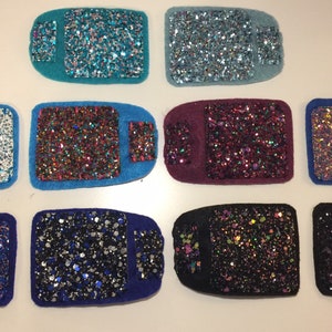 Può includere: Dieci quadrati di tessuto glitterato di diversi colori, ognuno con un colore e uno schema di glitter diversi. I quadrati sono disposti in due file di cinque.