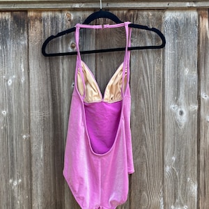 May include: A pink swimsuit with a halter neck and a low back. The swimsuit has a shimmery finish.