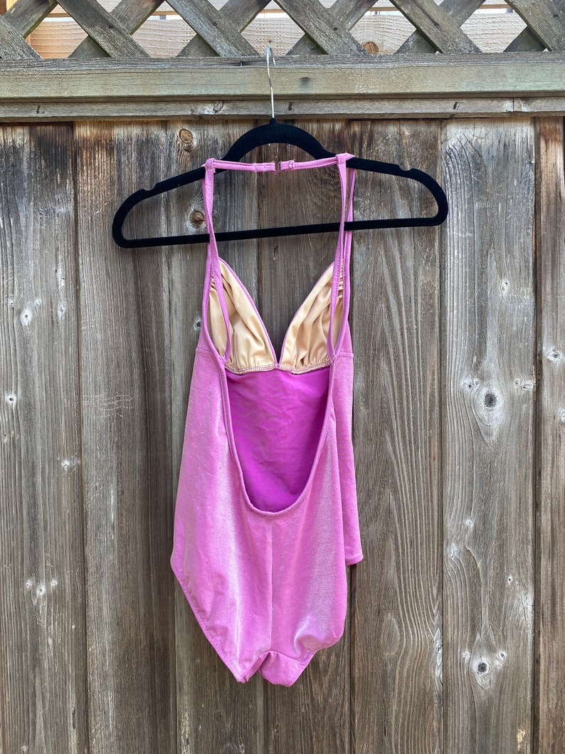 May include: A pink swimsuit with a halter neck and a low back. The swimsuit has a shimmery finish.