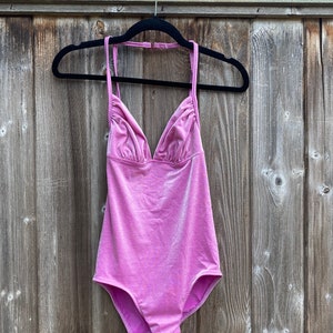 May include: A pink halter-style swimsuit with a V-neckline and a shiny finish.