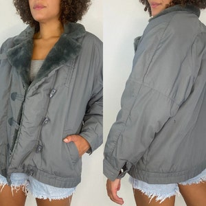 May include: A gray, quilted jacket with a faux fur collar. The jacket has a button closure and two pockets.