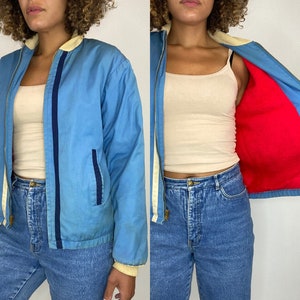 May include: A blue jacket with a white collar and red lining. The jacket has a zip closure and two pockets.