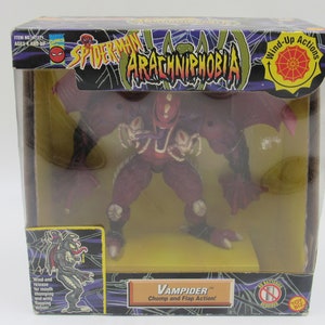 May include: A red and black action figure of a monster called Vampider from the Spider-Man: Arachnophobia toy line. The figure has wings, a large mouth, and a long tongue. The packaging features a spider web design and the text "Wind-Up Actions".