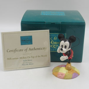 May include: A ceramic figurine of Mickey Mouse from the Disney Classics Collection. Mickey is standing on a colorful, patterned base. The figurine is in a box with a certificate of authenticity that reads "Millennium Mickey: On Top of the World".