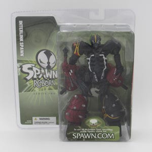 May include: A Spawn Reborn Series Two action figure in a plastic blister pack. The figure is black and red with green accents. The figure is holding a weapon in its right hand. The packaging has the Spawn Reborn logo and the text "Interlink Spawn".