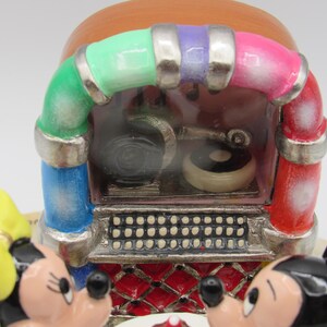 K&ouml;nnte beinhalten: Eine farbenfrohe Musikbox im Vintage-Stil mit Mickey und Minnie Mouse. Das Jukebox-Design hat einen roten, rosa, gr&uuml;nen, blauen und lila Bogen. Die Vorderseite der Jukebox hat eine silberne Lautsprecherblende und eine rot-wei&szlig; gemusterte Basis.