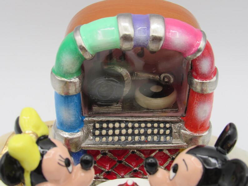 K&ouml;nnte beinhalten: Eine farbenfrohe Musikbox im Vintage-Stil mit Mickey und Minnie Mouse. Das Jukebox-Design hat einen roten, rosa, gr&uuml;nen, blauen und lila Bogen. Die Vorderseite der Jukebox hat eine silberne Lautsprecherblende und eine rot-wei&szlig; gemusterte Basis.