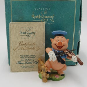May include: A ceramic figurine of a pig playing a fiddle. The pig is wearing a blue sailor hat and a blue and white sailor shirt. The figurine is part of a Walt Disney Classics Collection. The certificate of authenticity is included in the image.
