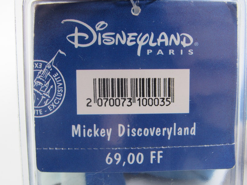 May include: A blue tag with the Disneyland Paris logo and the text "Mickey Discoveryland". The tag has a barcode and the text "Exclusive".