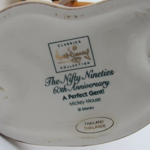 May include: A white ceramic figurine base with text that reads "The Nifty Nineties 60th Anniversary A Perfect Gent! Mickey Mouse." The figurine is part of the Walt Disney Classics Collection.