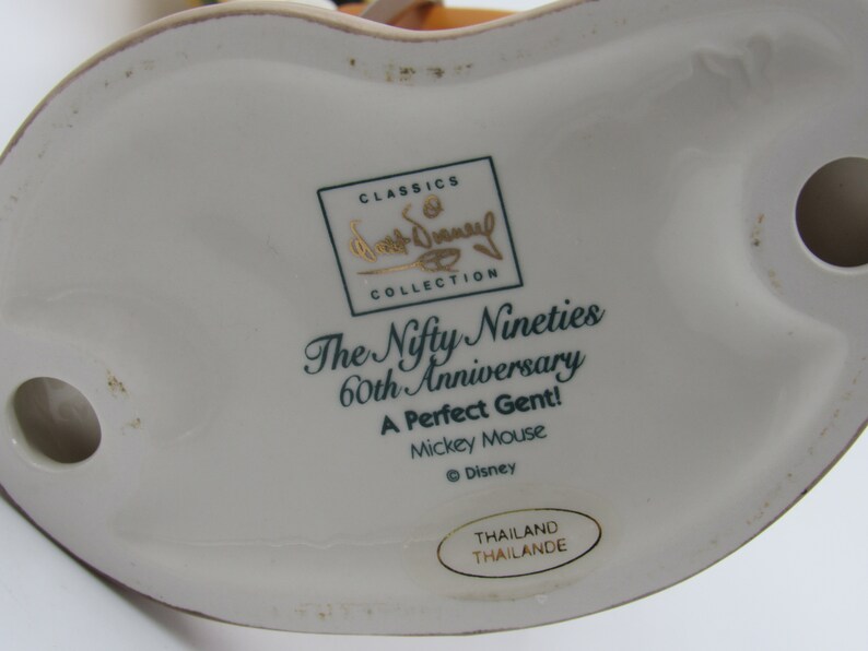 May include: A white ceramic figurine base with text that reads "The Nifty Nineties 60th Anniversary A Perfect Gent! Mickey Mouse." The figurine is part of the Walt Disney Classics Collection.