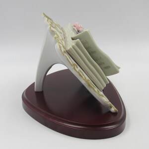 May include: A white porcelain music stand with a gold trim and a stack of sheet music. The stand is decorated with a pink and purple flower.