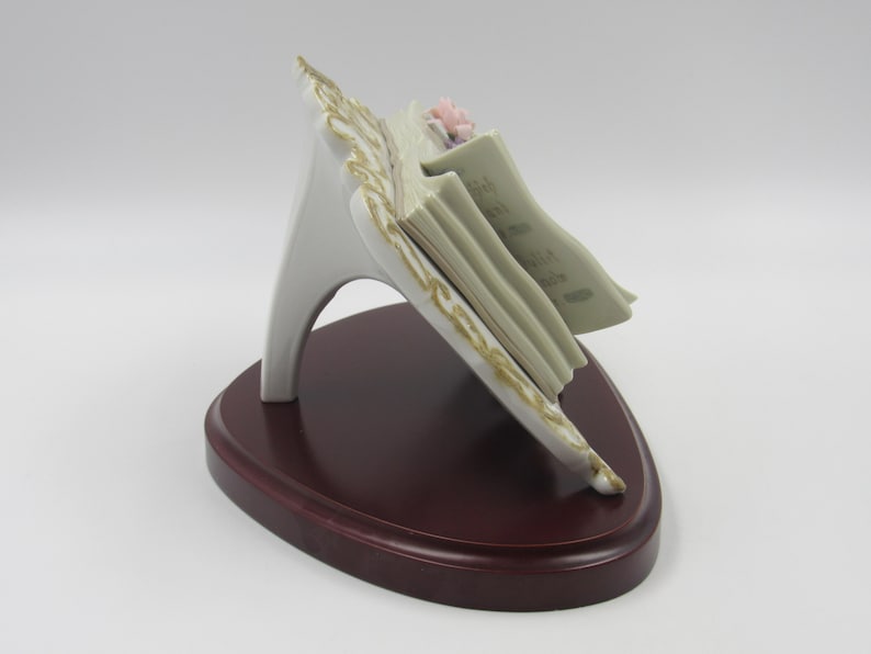 May include: A white porcelain music stand with a gold trim and a stack of sheet music. The stand is decorated with a pink and purple flower.