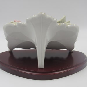 May include: A white porcelain figurine of a floral arrangement with pink and yellow flowers. The figurine is on a wooden base.