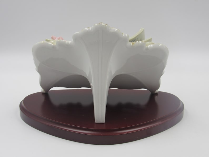 May include: A white porcelain figurine of a floral arrangement with pink and yellow flowers. The figurine is on a wooden base.