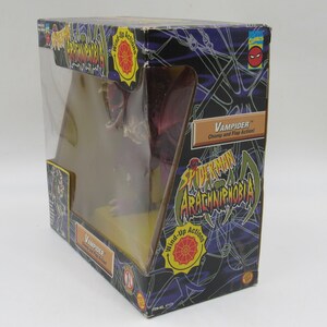 May include: A red and brown wind-up toy spider with the name "Vampider" and the text "Chomp and Flap Action!" on the box. The box is black with a spider web design and the words "Spider-Man Arachniphobia" on it.