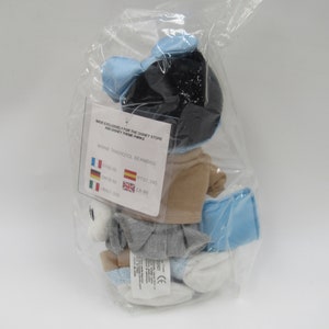 May include: A blue and white Minnie Mouse beanbag plush toy in a plastic bag. The tag reads "Made exclusively for the Disney Store and Disney Theme Parks" and "Minnie Traditionel Beanbag". The price is listed in Euros, US Dollars, British Pounds, and Spanish Pesetas.