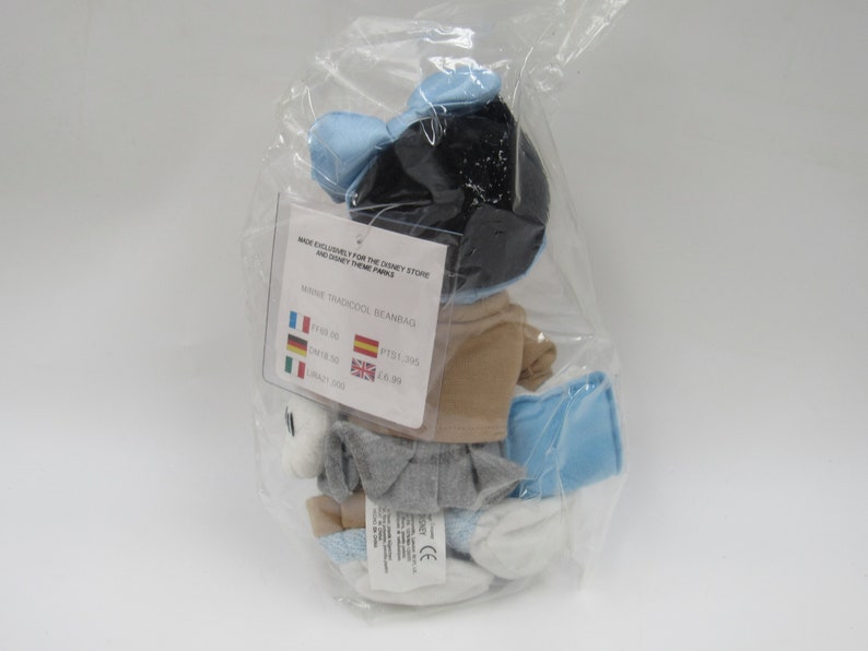 May include: A blue and white Minnie Mouse beanbag plush toy in a plastic bag. The tag reads "Made exclusively for the Disney Store and Disney Theme Parks" and "Minnie Traditionel Beanbag". The price is listed in Euros, US Dollars, British Pounds, and Spanish Pesetas.