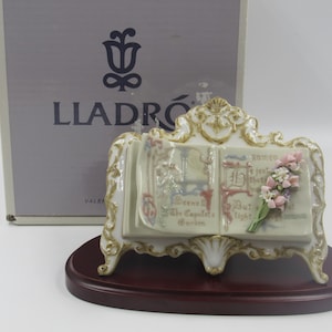 May include: A porcelain figurine of an open book with a bouquet of flowers on the right page. The book is on a wooden stand with ornate details. The figurine is made by Lladr&oacute;.