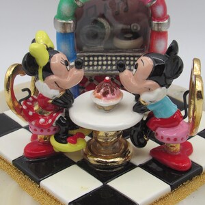 K&ouml;nnte beinhalten: Figur von Mickey und Minnie Mouse an einem Tisch mit einem Cupcake, vor einer Jukebox. Minnie tr&auml;gt ein rotes Polka-Dot-Kleid und Mickey ein blaues Hemd. Die Basis ist ein schwarz-wei&szlig;es Schachbrettmuster.