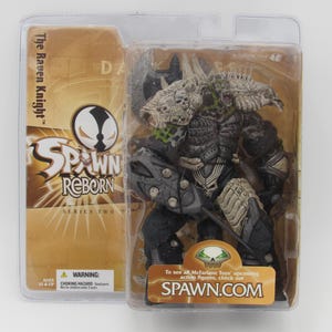 以下が含まれることがあります： Spawn Reborn シリーズ2 のアクションフィギュア、The Raven Knight。フィギュアは黒とグレーで、骨のようなヘルメットと大きな剣を装備している。パッケージはゴールドとブラックで、Spawn Reborn のロゴがデザインされている。