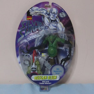May include: A plastic package containing a green action figure of a Meekan Alien from the 1995 Silver Surfer 30th Anniversary Series. The figure comes with an Earth Tremor Detector. The package also features a silver action figure of the Silver Surfer.